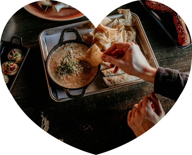 Hands dipping a chip into a skillet of queso