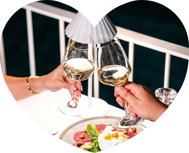 Two people toasting wine glasses at dinner